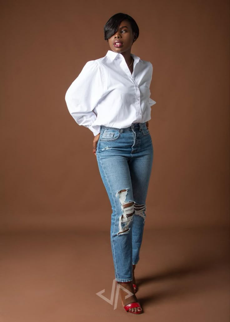 a woman in ripped jeans and a white shirt poses for the camera with her hands on her hips