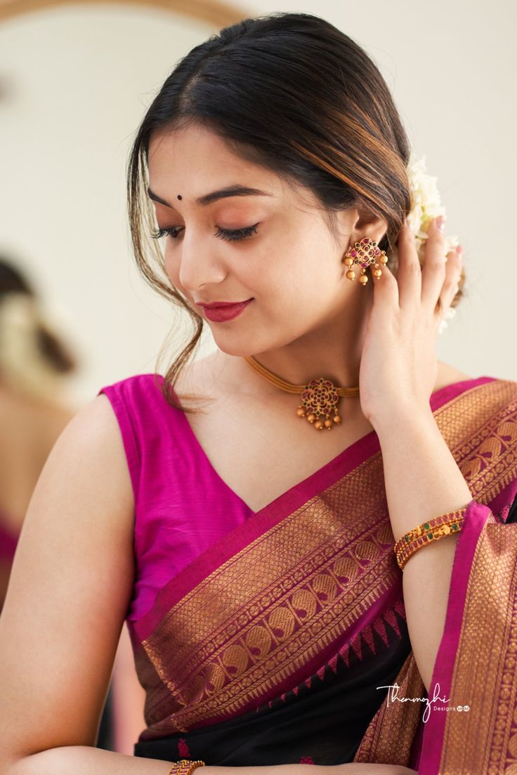 a woman in a pink and black saree holding her hand up to her ear