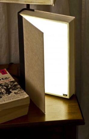 a lamp sitting on top of a wooden table next to a book and a pillow