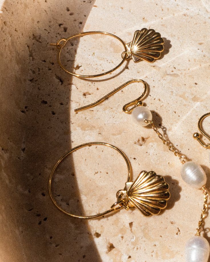 You've just discovered your lightweight summer hoop for the summer. Featuring high-quality gold hoops with a stunning seashell charm, these are the perfect size to never take off. Shop the matching necklace here. 14k Gold Fill Hoop Drop: 2" Sold as a pair 14k Gold Filled Hoop Charms Jewelry, Ocean-inspired Gold Sterling Silver Jewelry, Yellow Gold-plated Hoop Earrings With Pearl Charm, Gold Pearl Drop Jewelry For Summer, Gold Sterling Silver Jewelry For Summer, Elegant Shell-shaped Brass Jewelry, Single Shell-shaped Gold Earring, Summer Gold Jewelry With Pearl Charm, Yellow Gold Shell Jewelry For Beach