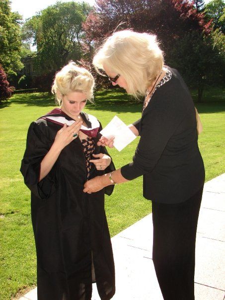 two women in graduation gowns are looking at something on the ground while one woman is holding a piece of paper