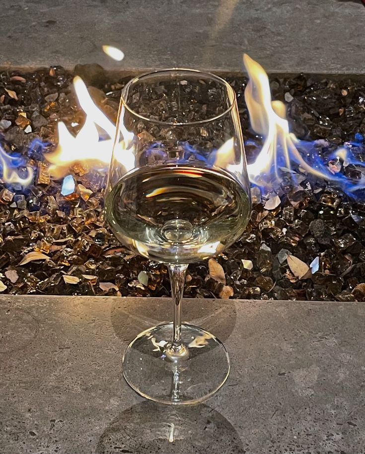 a glass of wine sitting on top of a table next to a fire place with rocks and gravel