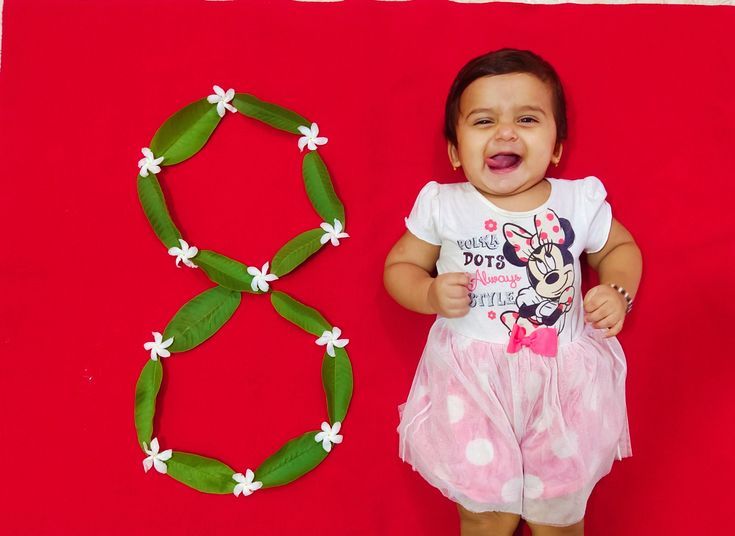 a baby girl standing in front of a paper wreath and an ornament with a minnie mouse on it