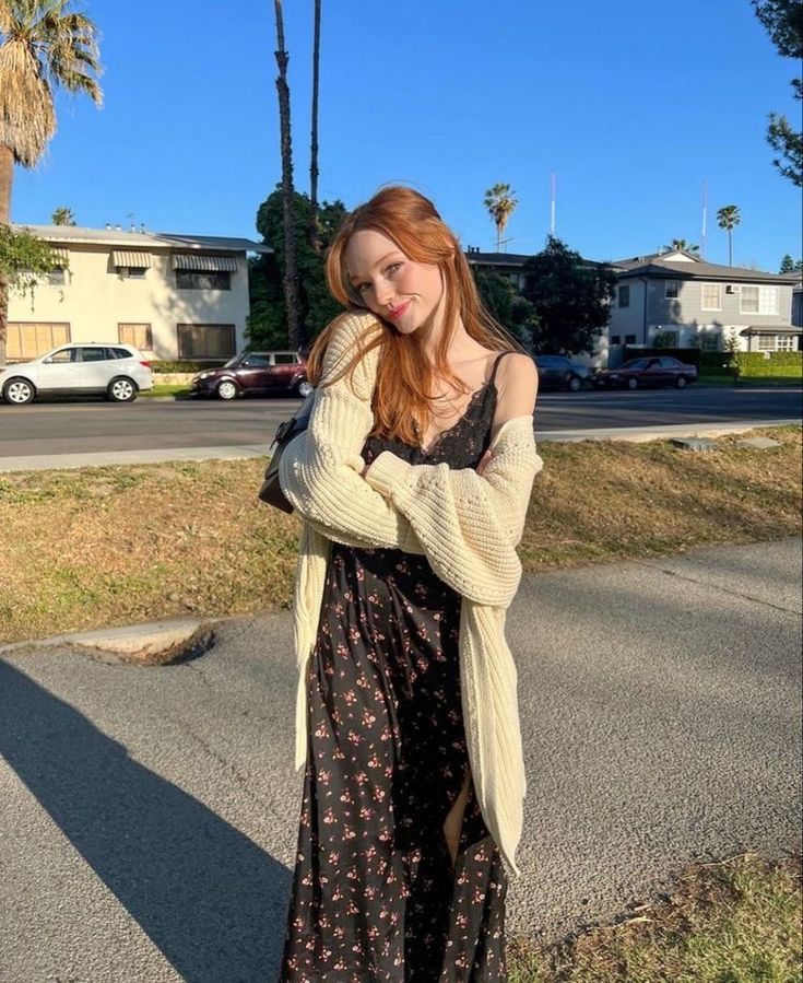 a woman standing on the side of a road wearing a long dress and cardigan