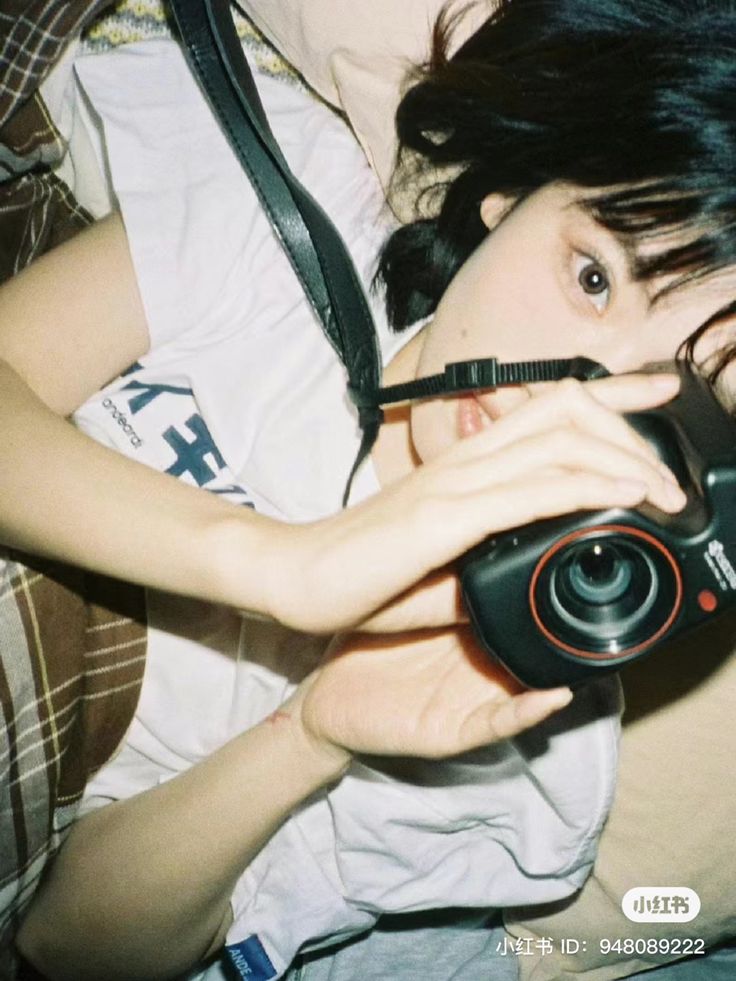 a woman laying on top of a bed holding a camera