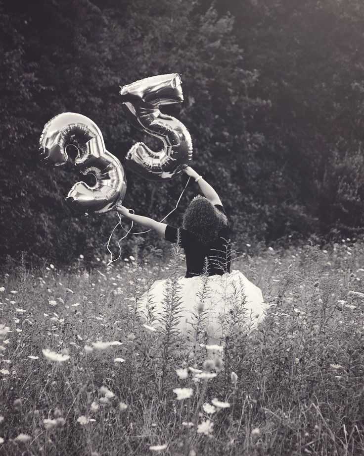 a woman sitting in a field holding onto some balloons that are shaped like the number five