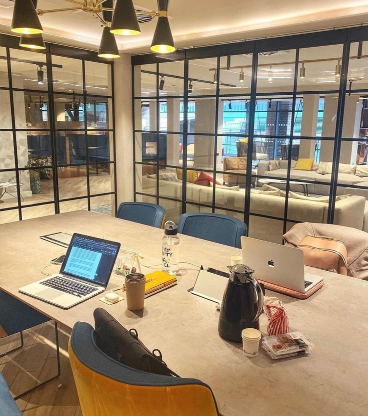 a table with two laptops on it in front of large windows and couches