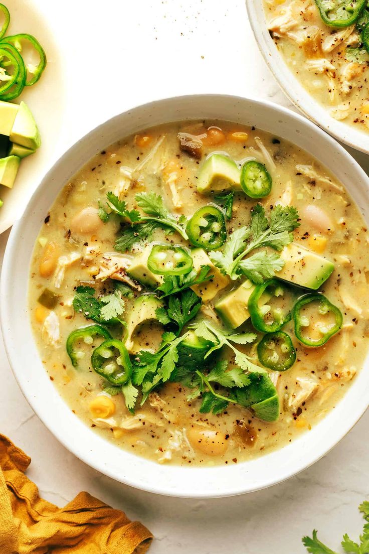 two bowls filled with soup and garnished with cilantro, jalapenos, and green onions