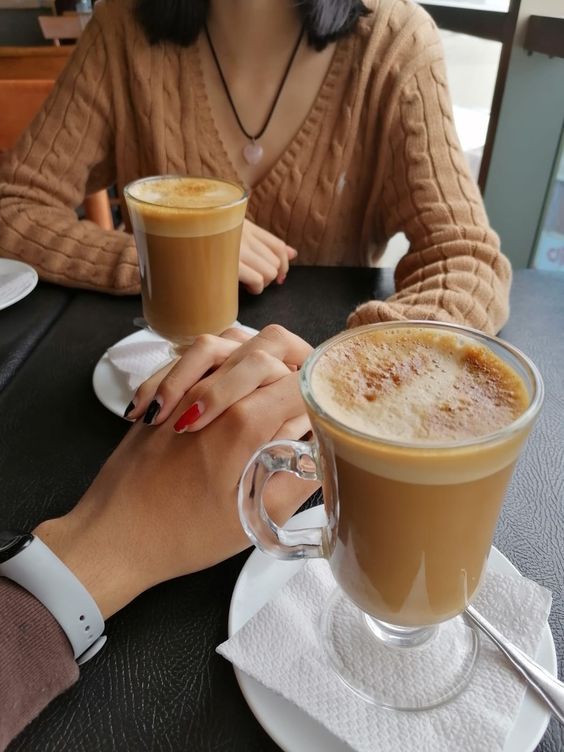 two people sitting at a table with drinks in front of them, one holding the other's hand