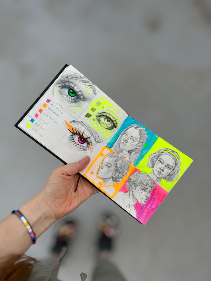 a hand holding an open book with drawings on it's cover and the pages are colored multicolored