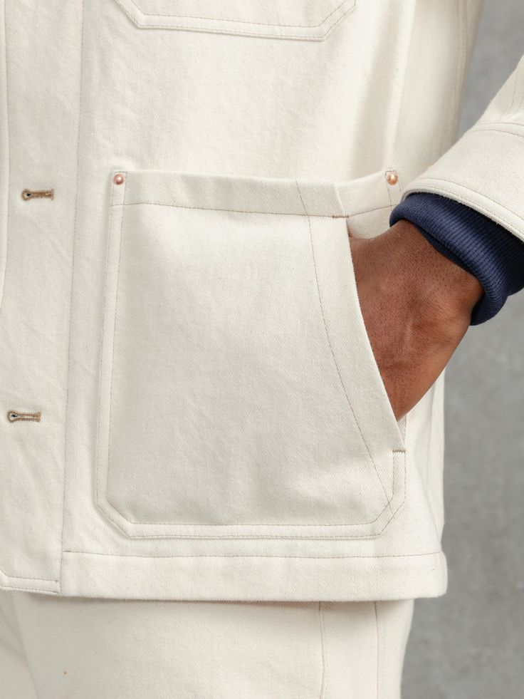 a close up of a person wearing a white jacket and blue tie with his hand in the pocket