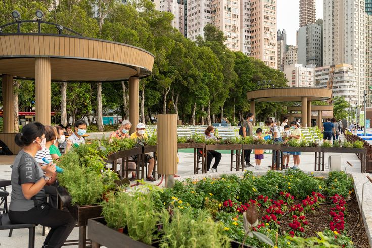 many people are sitting at tables in the park with lots of plants and flowers around them