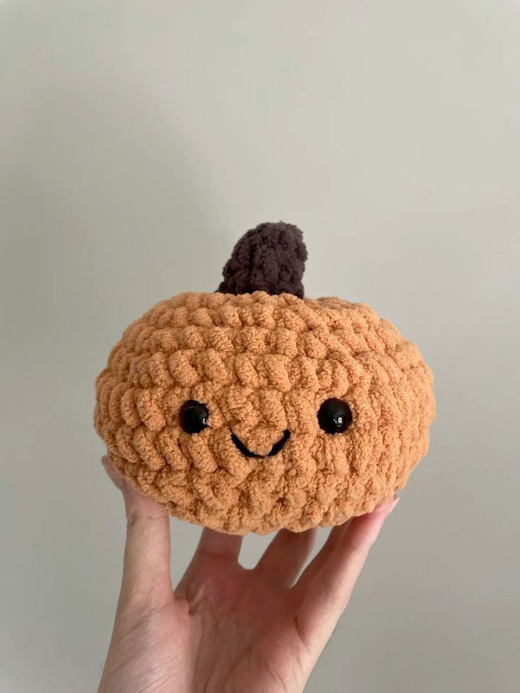 a hand holding a small crocheted pumpkin with a black top on it's head