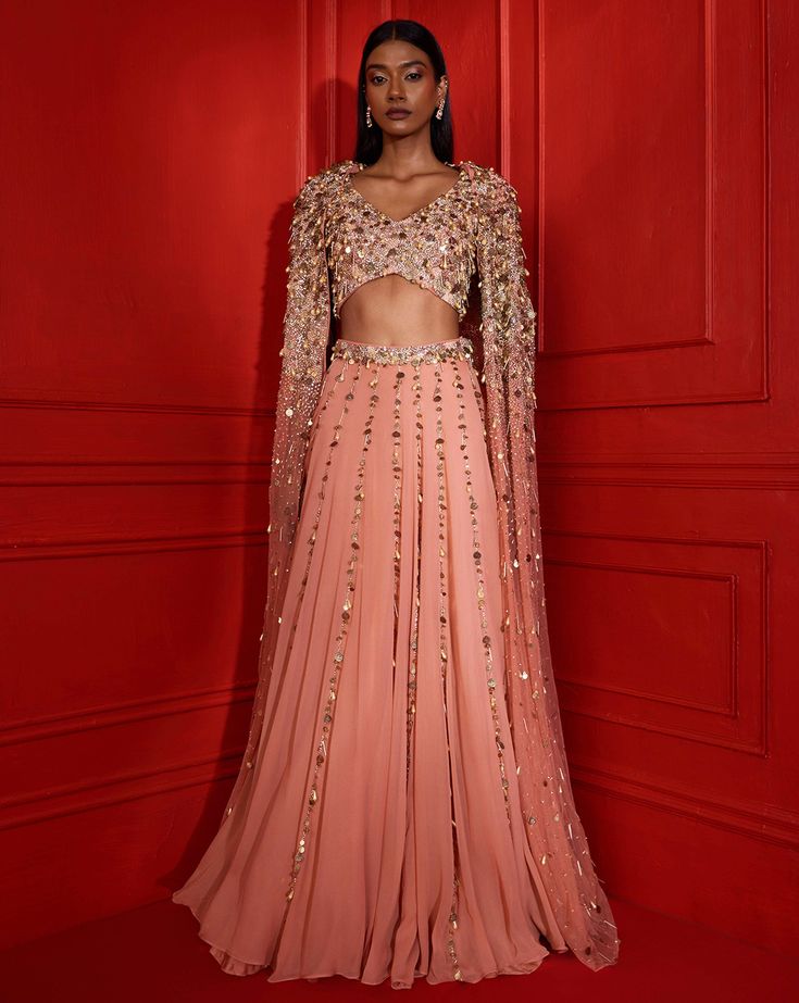 Dusty peach flowy lehenga hand embellished with our coin & pearl embellishment in a linear format, with a heavily embellished waist band. Paired with a coin & pearl embellished sleeveless crop & a heavily embellished matching net cape with power shoulders.From Shloka Khialani's Afterglow CollectionDELIVERY TIMEPlease allow 8-12 weeks for your outfit to arrive.FABRIC DETAILSGeorgette, Net, CrepeSpot Dry Clean Only. Open Image, Us Coins, Coin Pearls, Lehenga