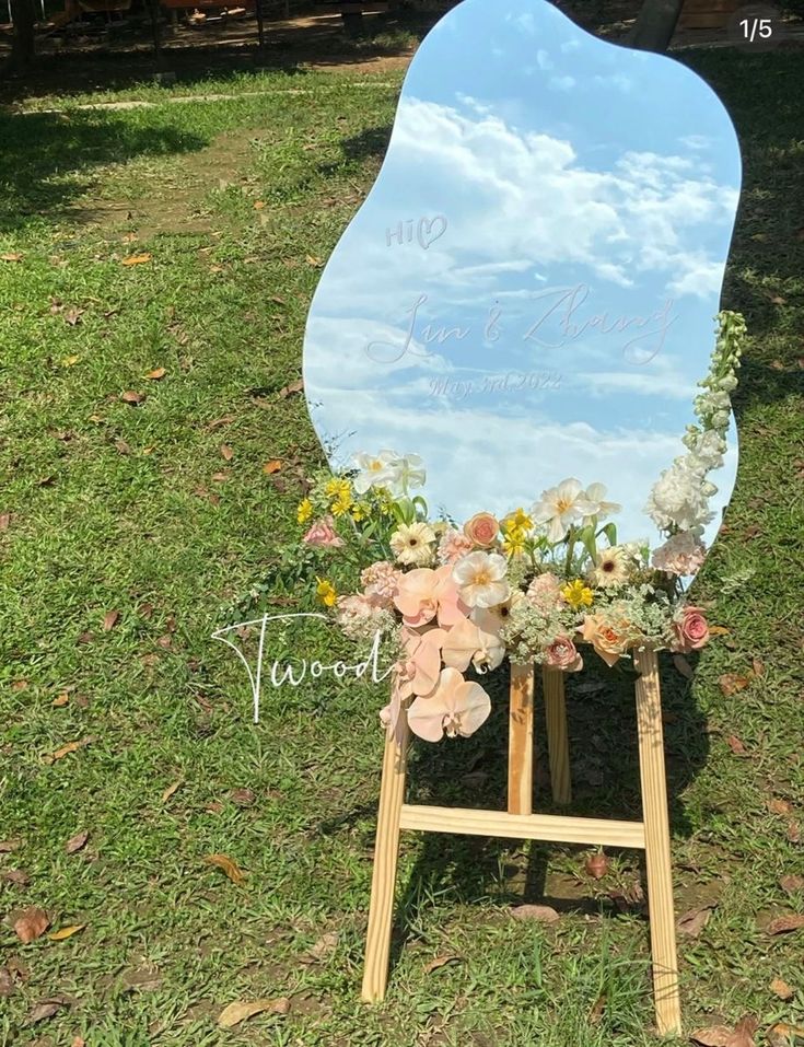 a large mirror sitting on top of a wooden easel with flowers in front of it