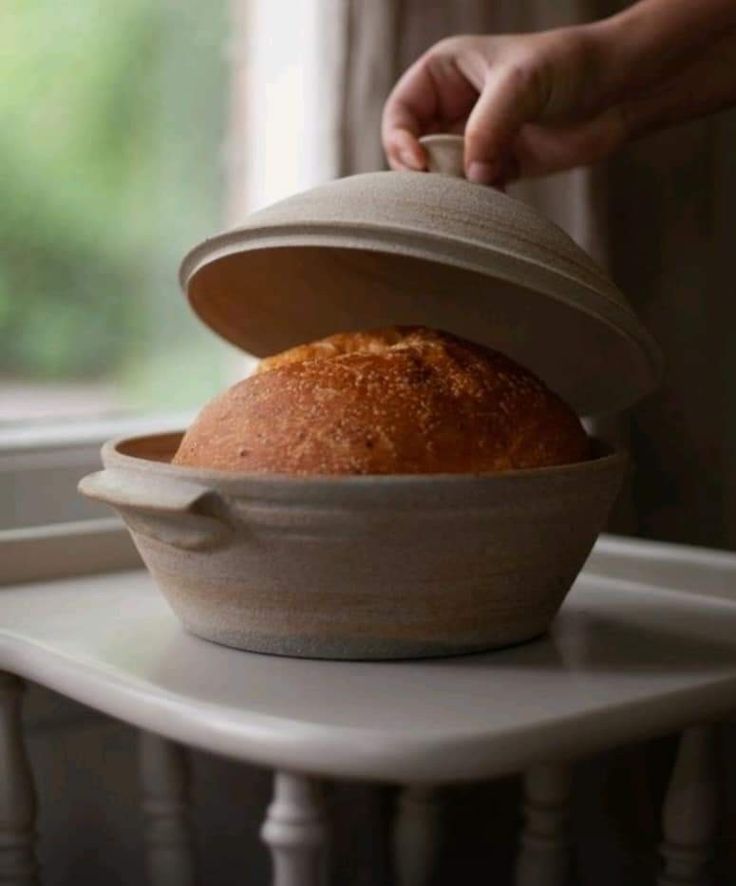 a loaf of bread sitting in a bowl on top of a white table next to a window