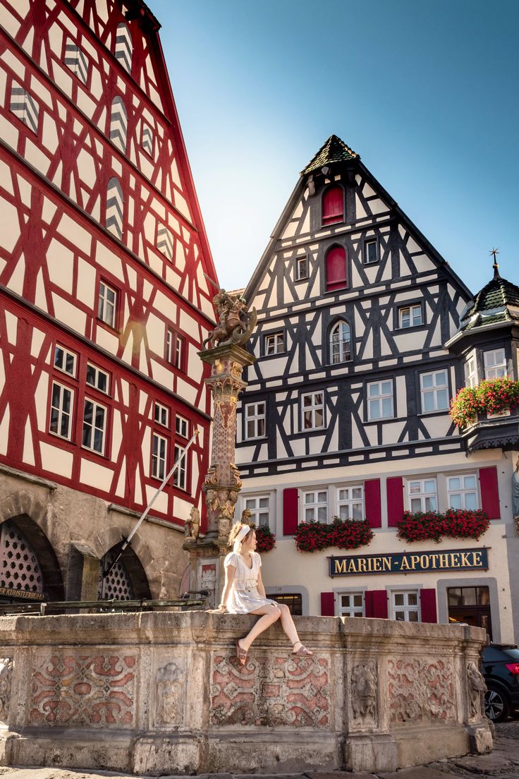 a woman is sitting on a wall in front of some buildings with red shutters