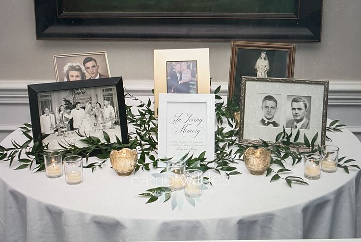 a table topped with pictures and candles on top of a white cloth covered round table