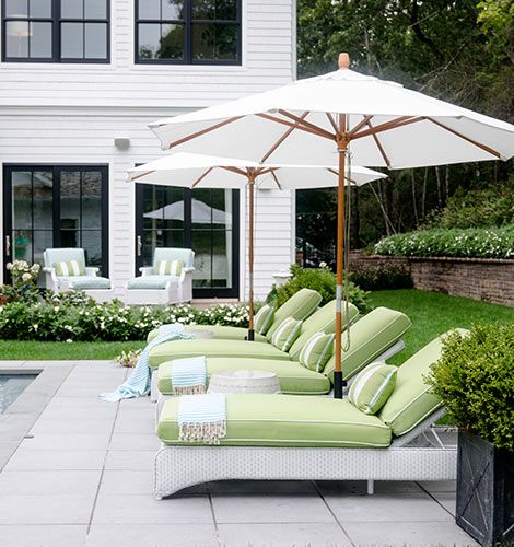 an outdoor patio with lounge chairs and umbrellas in front of a large white house