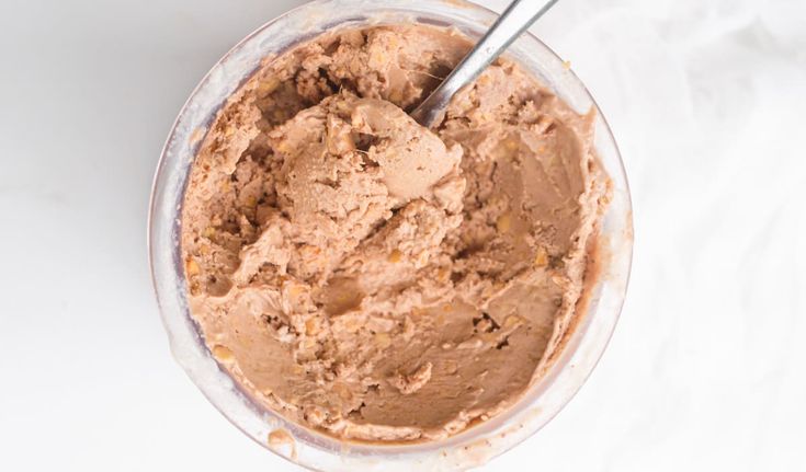 a bowl filled with chocolate ice cream on top of a white tablecloth next to a spoon