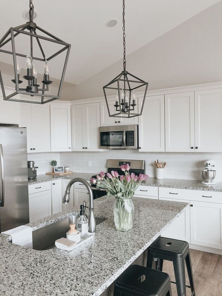 a kitchen with white cabinets and granite counter tops, two pendant lights hanging over the island