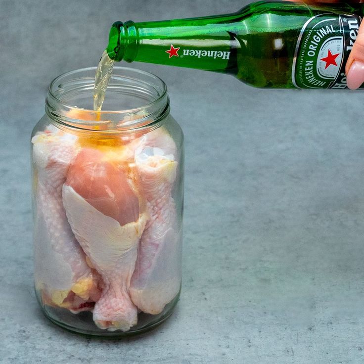 a person pours beer into a jar filled with raw chicken