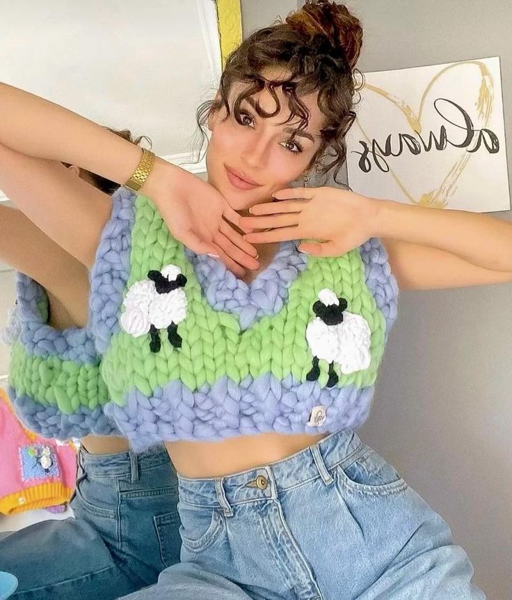 a woman is sitting on the floor with her arms behind her head while wearing a knitted top