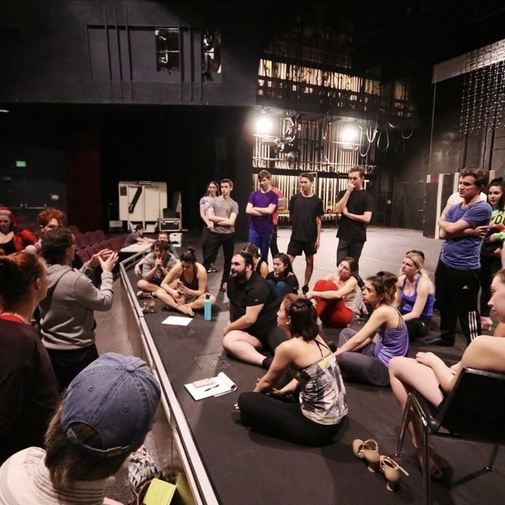 a group of people sitting on the floor in front of a stage with microphones