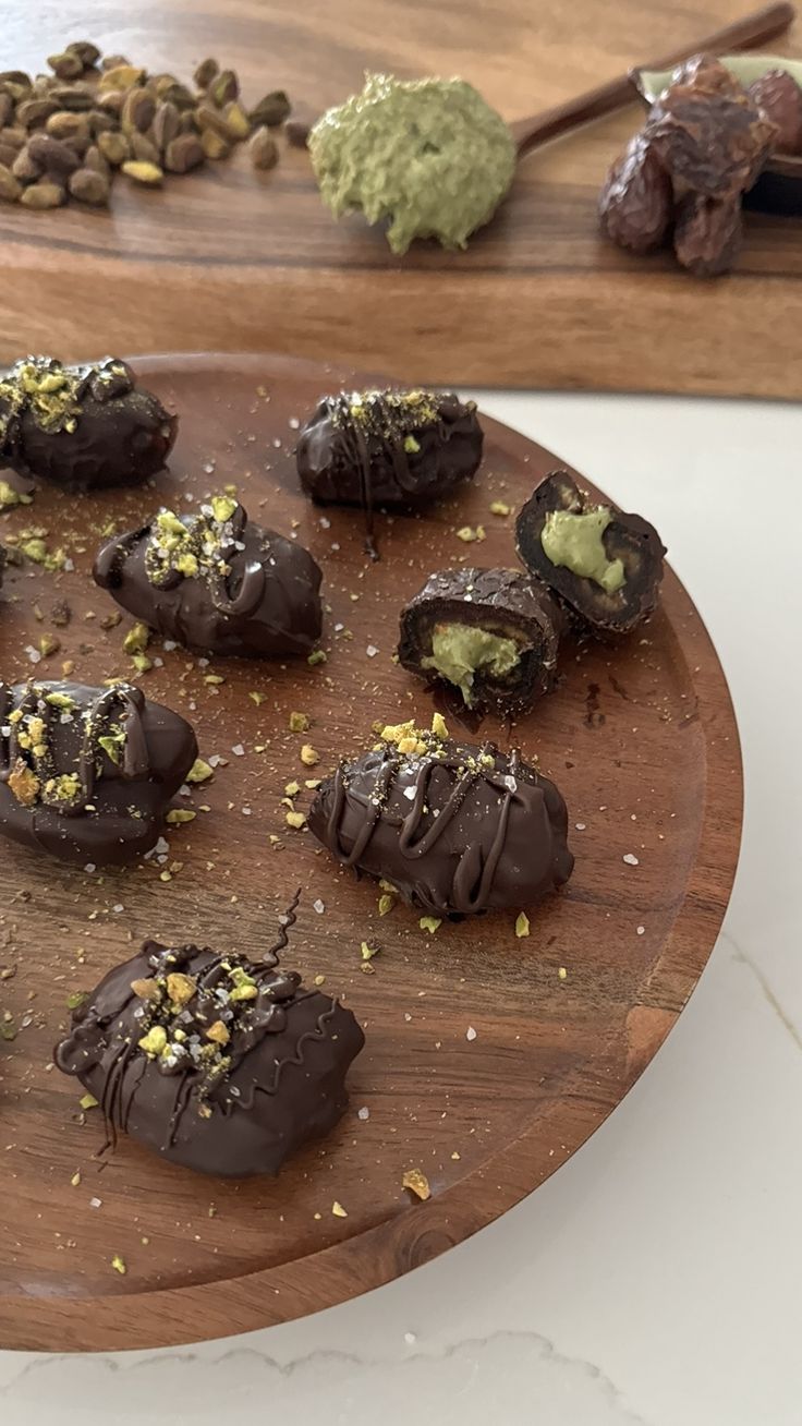 there are many chocolates on the wooden platter with nuts and pistachio