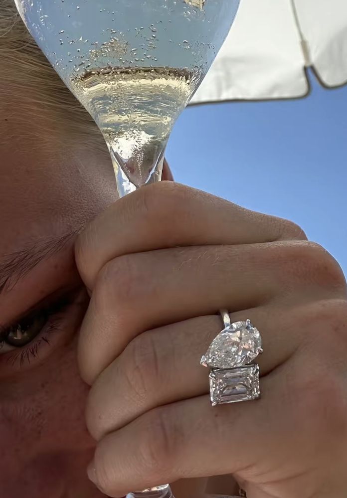 a close up of a person holding a wine glass with a diamond ring on it