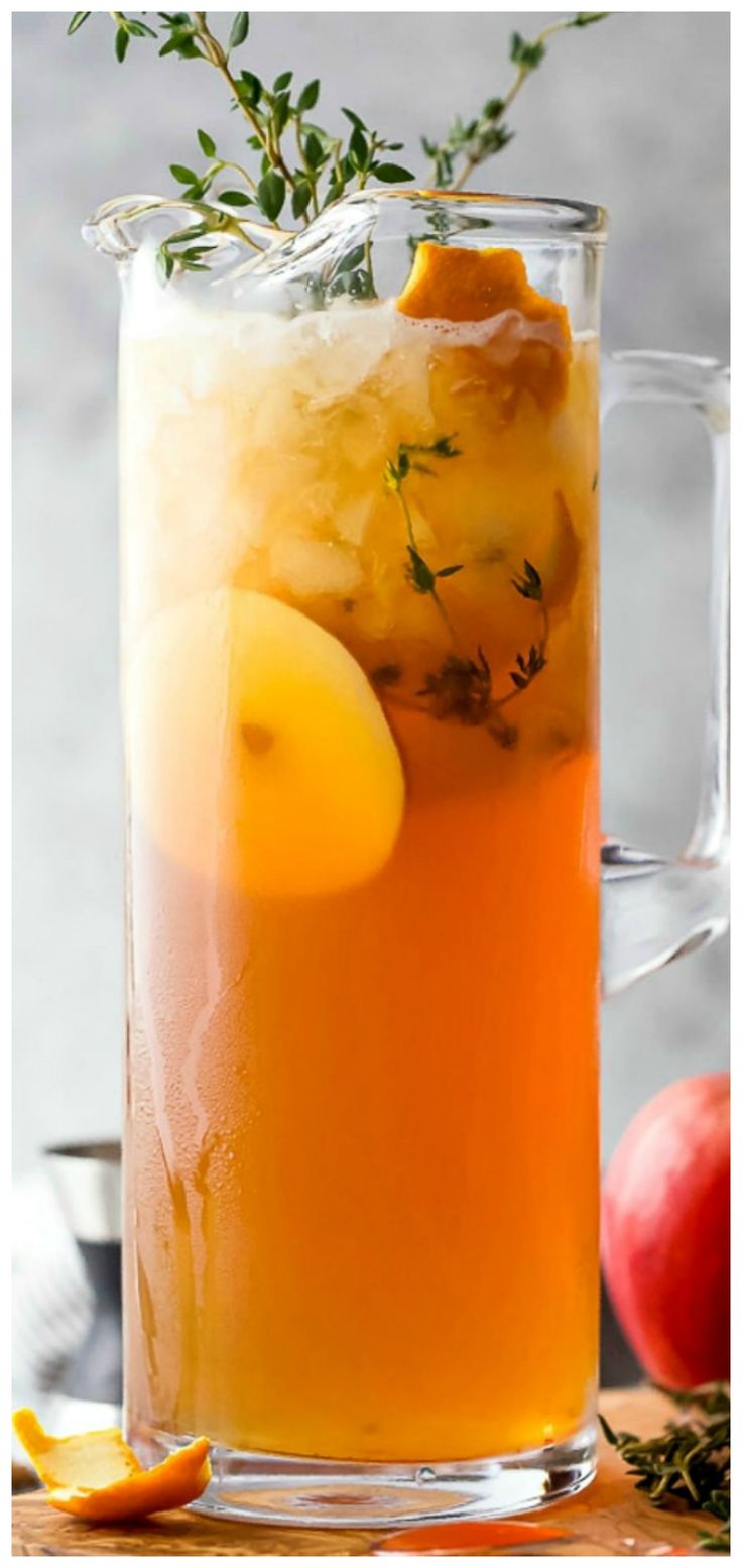 a pitcher filled with orange juice and lemon wedges next to an apple on the side