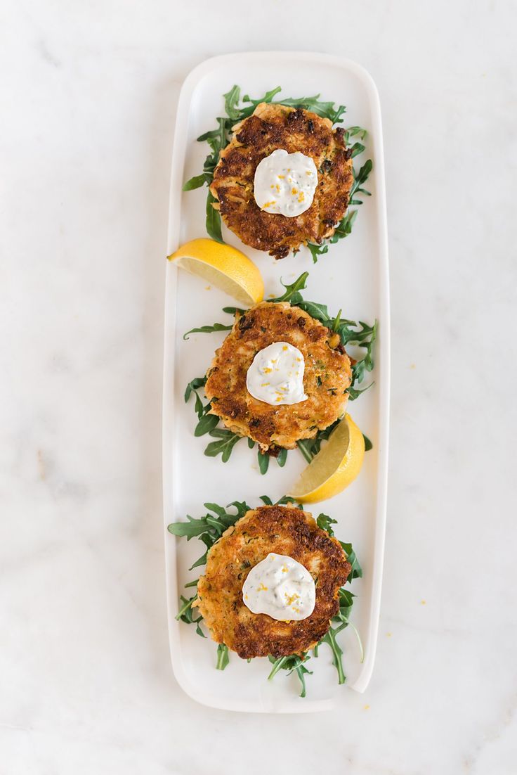 three crab cakes on a plate with lemon wedges and parmesan cheese sauce