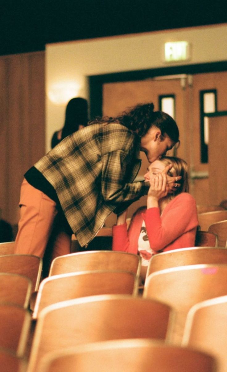 a man kneeling down next to a woman on top of a wooden chair in front of an audience