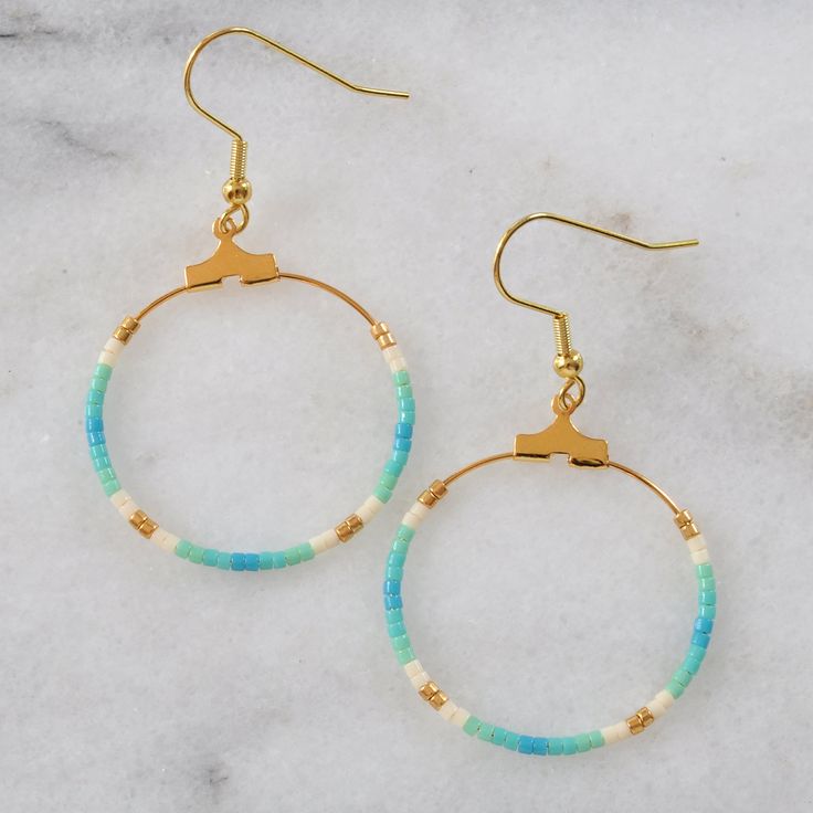 Your soon-to-be favorites, these small gold beaded hoops (available in 22 exclusive patterns) are perfect for day, night and well, everything in between. gold-plated hoop and hooks lead-free and nickel-free glass seed beads plastic earring back 1.25" in diameter and overall length is 2" from top of hook packaged on a hand-stamped kraft earring card in a clear resealing bag EXCLUSIVE STYLES NAVY Navy blue, bronze, and blush PHOENIX Turquoise, red, cream, and gold GREY Matte black, metallic pink, Nickel Free Summer Hoop Earrings, Nickel-free Circle Hoop Earrings For Summer, Summer Nickel Free Hoop Earrings, Summer Nickel-free Hoop Earrings, Gold Beaded Hoop Earrings For The Beach, Dangle Hoop Earrings With Tiny Beads For Beach, Beaded 14k Gold Filled Hoop Earrings, Trendy Summer Hoop Earrings With Tiny Beads For Beach, Gold Hoop Earrings With Colorful Beads For Beach