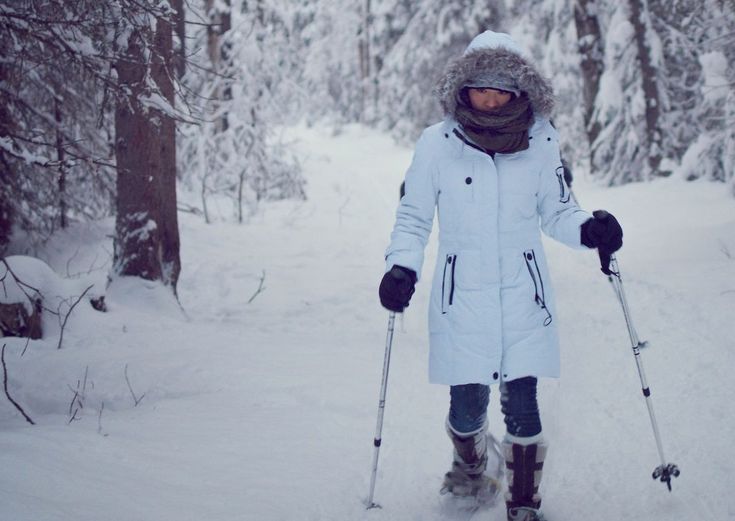 a woman in white coat on skis walking through snow covered ground with trees behind her