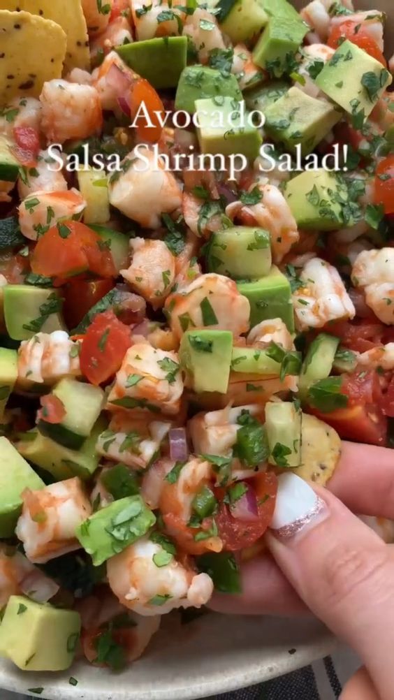 someone is holding up a salad with shrimp, avocado and tomatoes in it