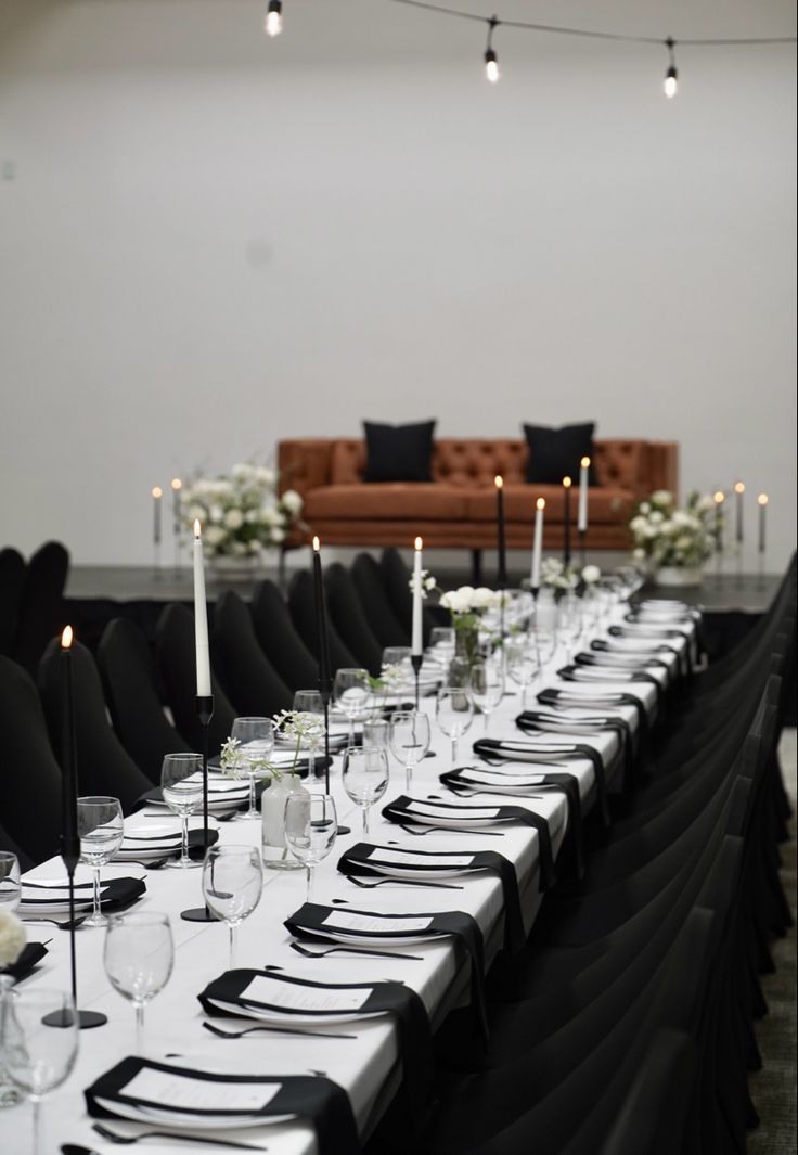 a long table is set up with black and white place settings for an elegant dinner