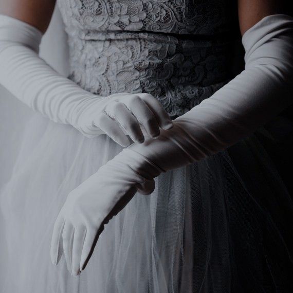 a woman wearing white gloves and holding her hands behind her back in black and white