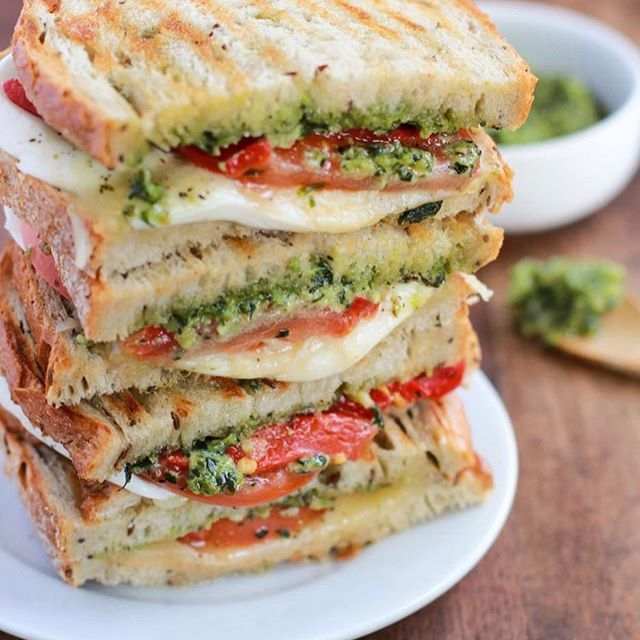 a stack of grilled sandwiches with pesto and tomato on them sitting on a white plate