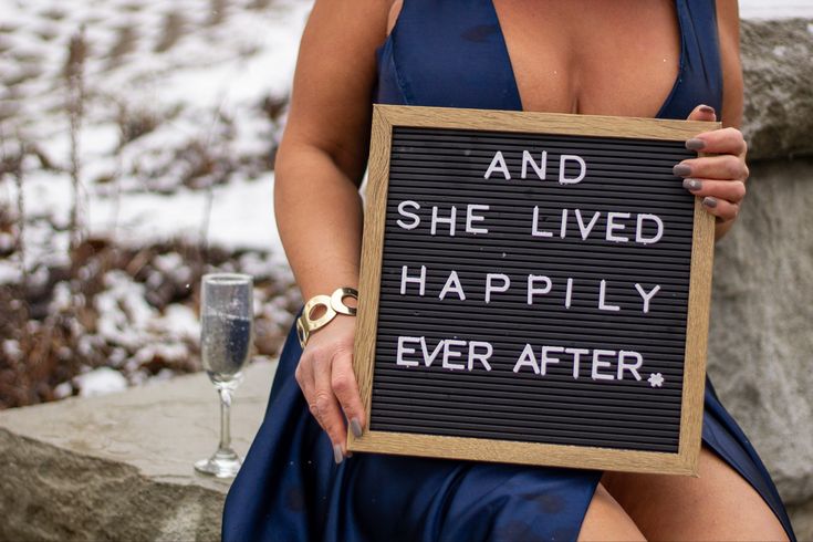 a woman holding up a sign that says and she lived happily ever after with champagne in the background