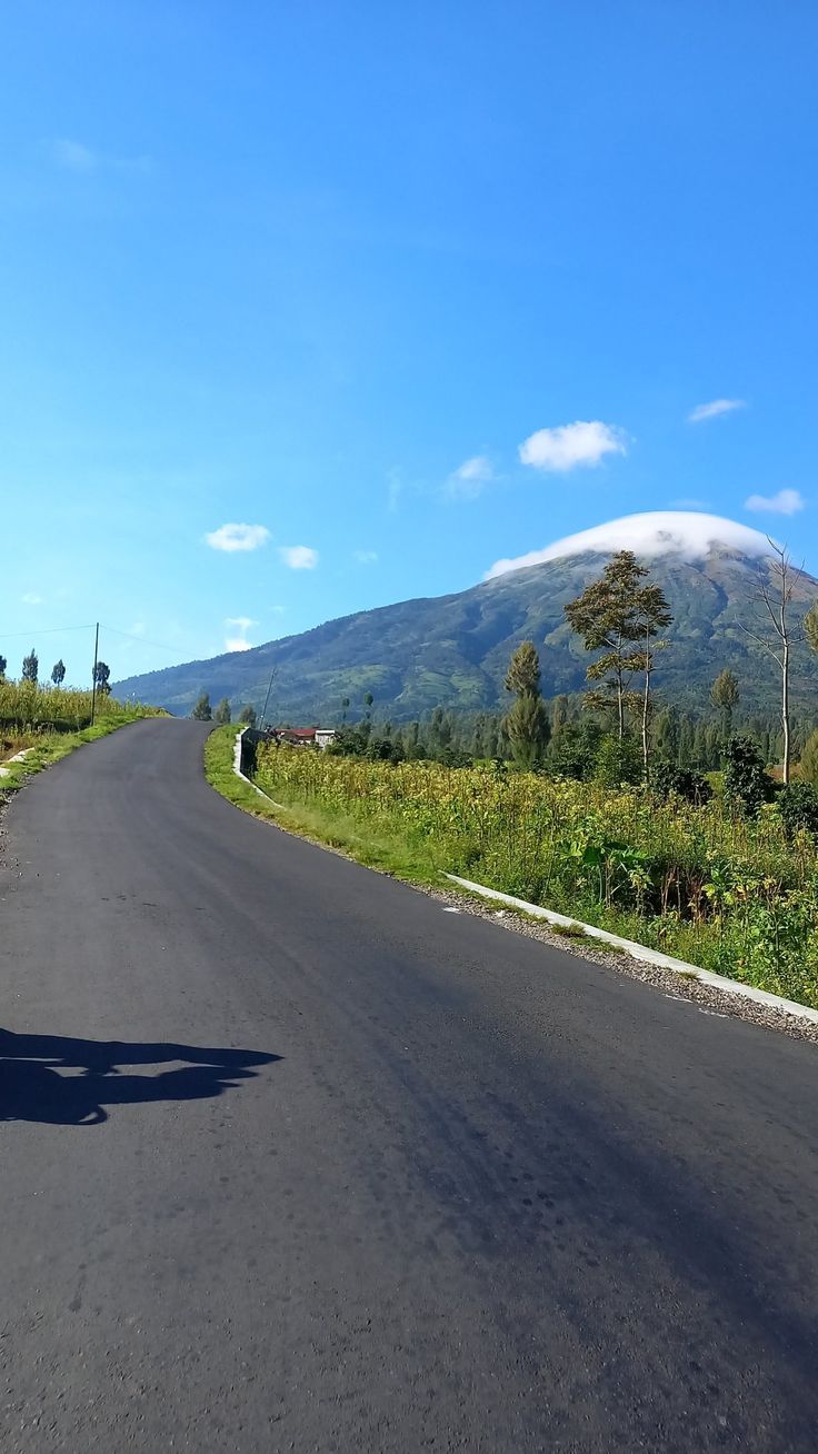 a person riding a motorcycle down the middle of a road with a mountain in the background