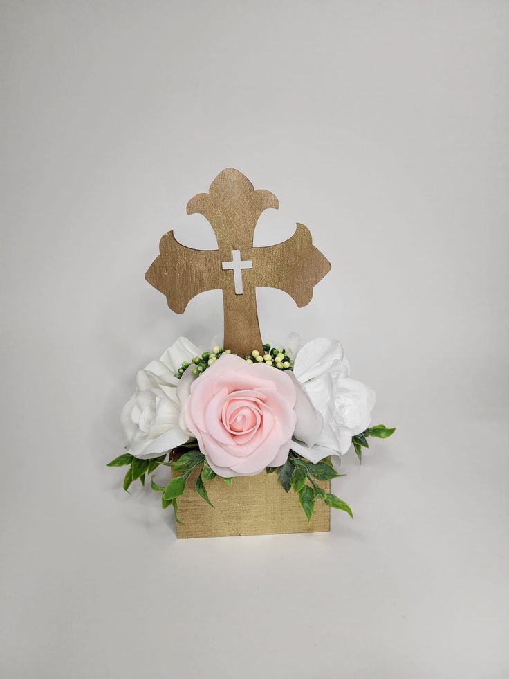 a wooden cross with white and pink flowers in it on top of a table next to a wall