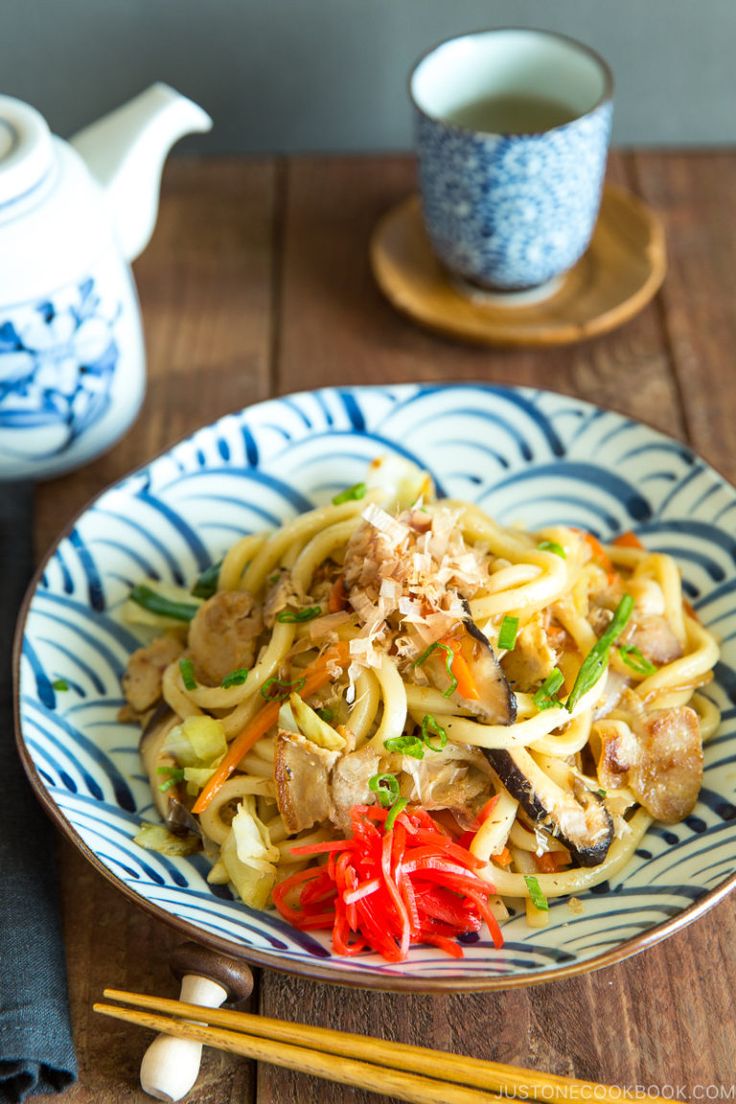 a bowl filled with noodles and vegetables next to chopsticks on a wooden table