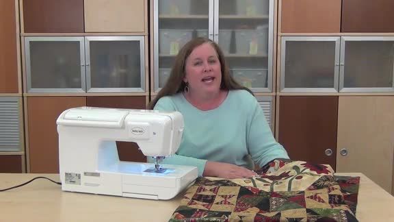 a woman sitting at a table in front of a sewing machine and quilting material