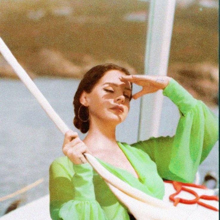 a woman sitting on top of a boat holding her hand to her head and looking off into the distance