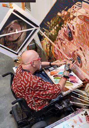 a man sitting in a wheel chair painting on an easel next to some paintings