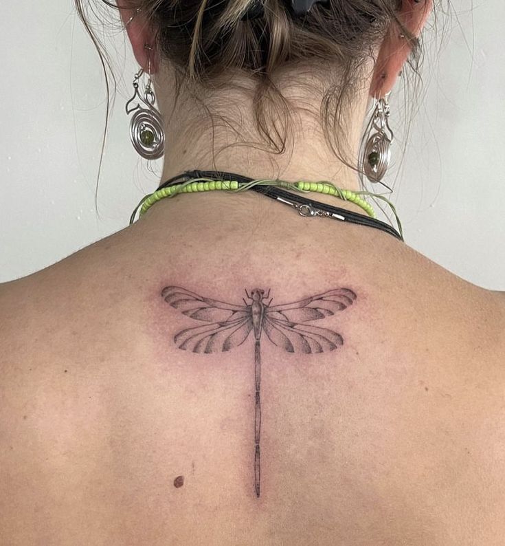 a woman with a tattoo on her back has a dragonfly tattooed on her shoulder