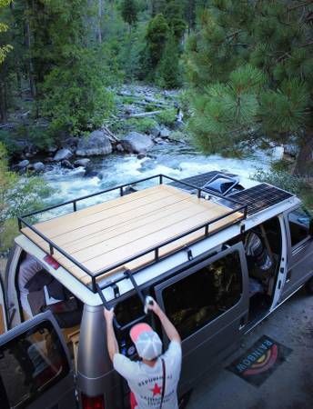 a man standing in the back of a van next to a river and forest area