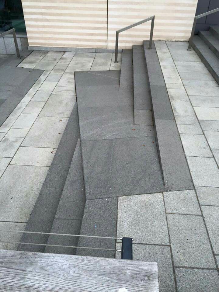 a wooden bench sitting on top of a cement floor next to a building with stairs