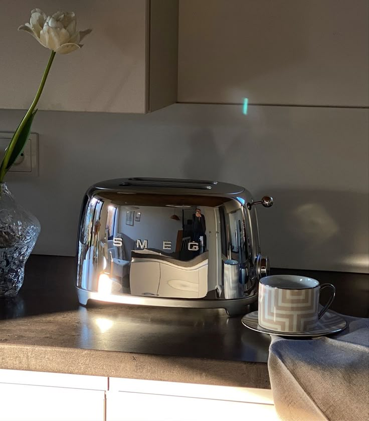 a silver toaster sitting on top of a counter next to a vase with flowers